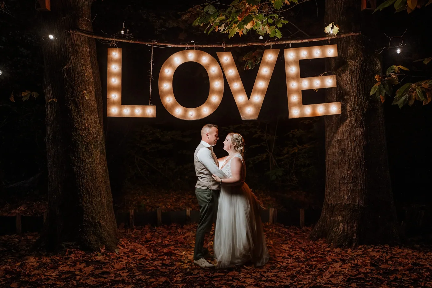 Bruidspaar danst 's avonds onder verlichte LOVE-letters, gefotografeerd door TWP Weddings
