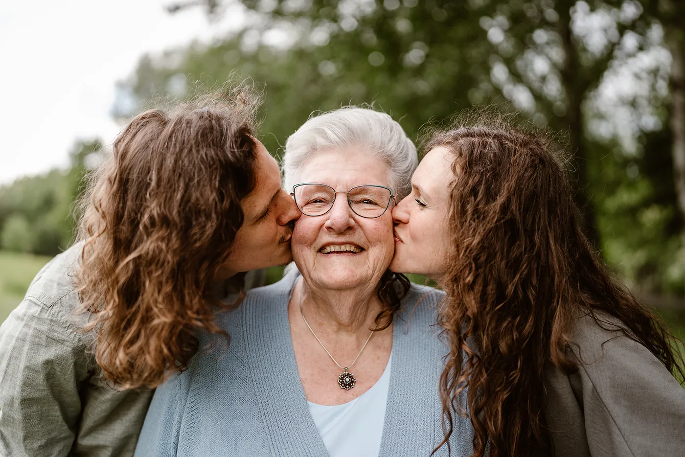 Twee vrouwen geven tegelijk een kus op de wang van de oudste van de familie