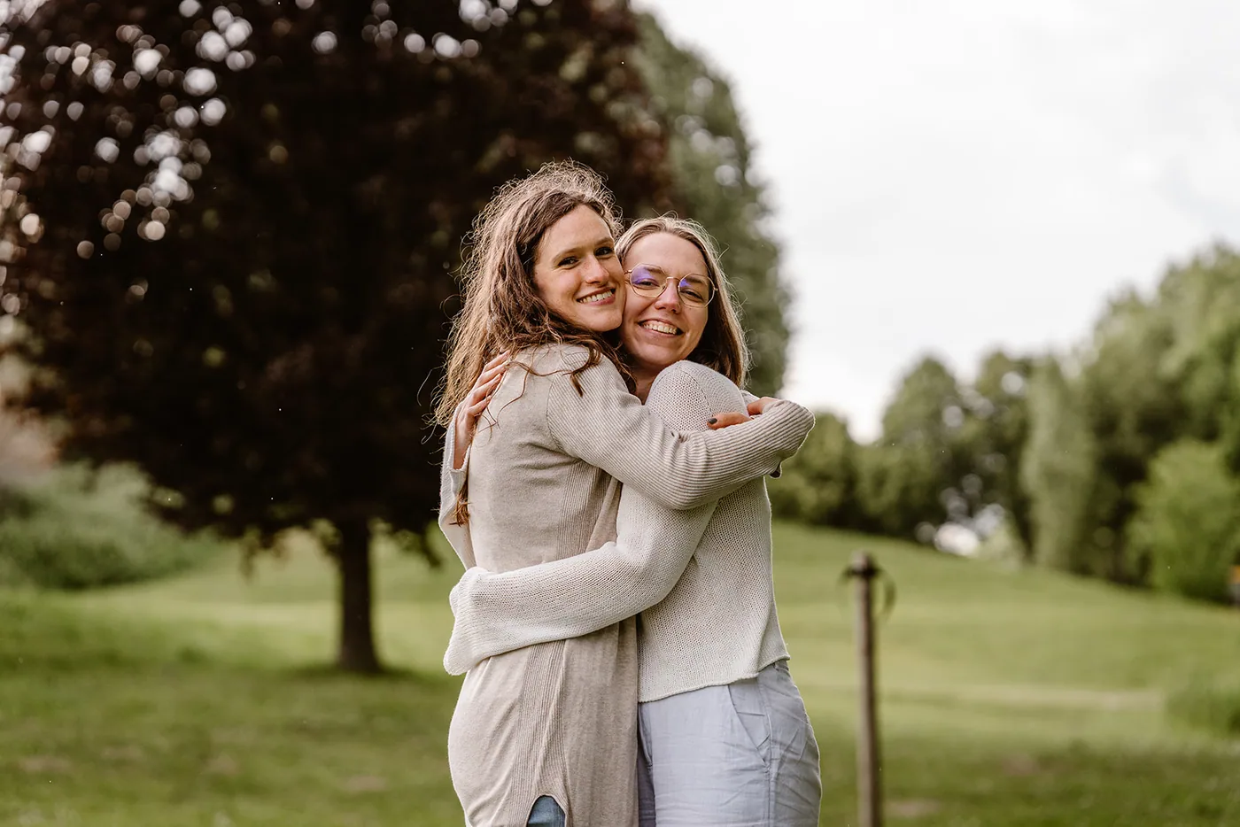 Twee vrouwen omhelzen elkaar lachend onder een boom