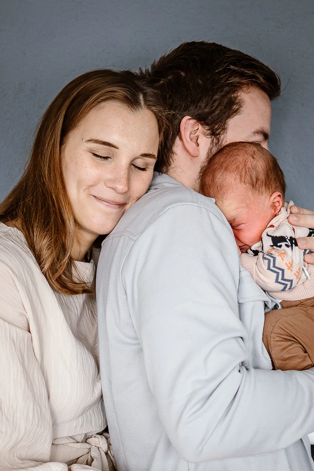 Twee ouders liggen wang aan wang met hun pasgeboren kind tussen hen in