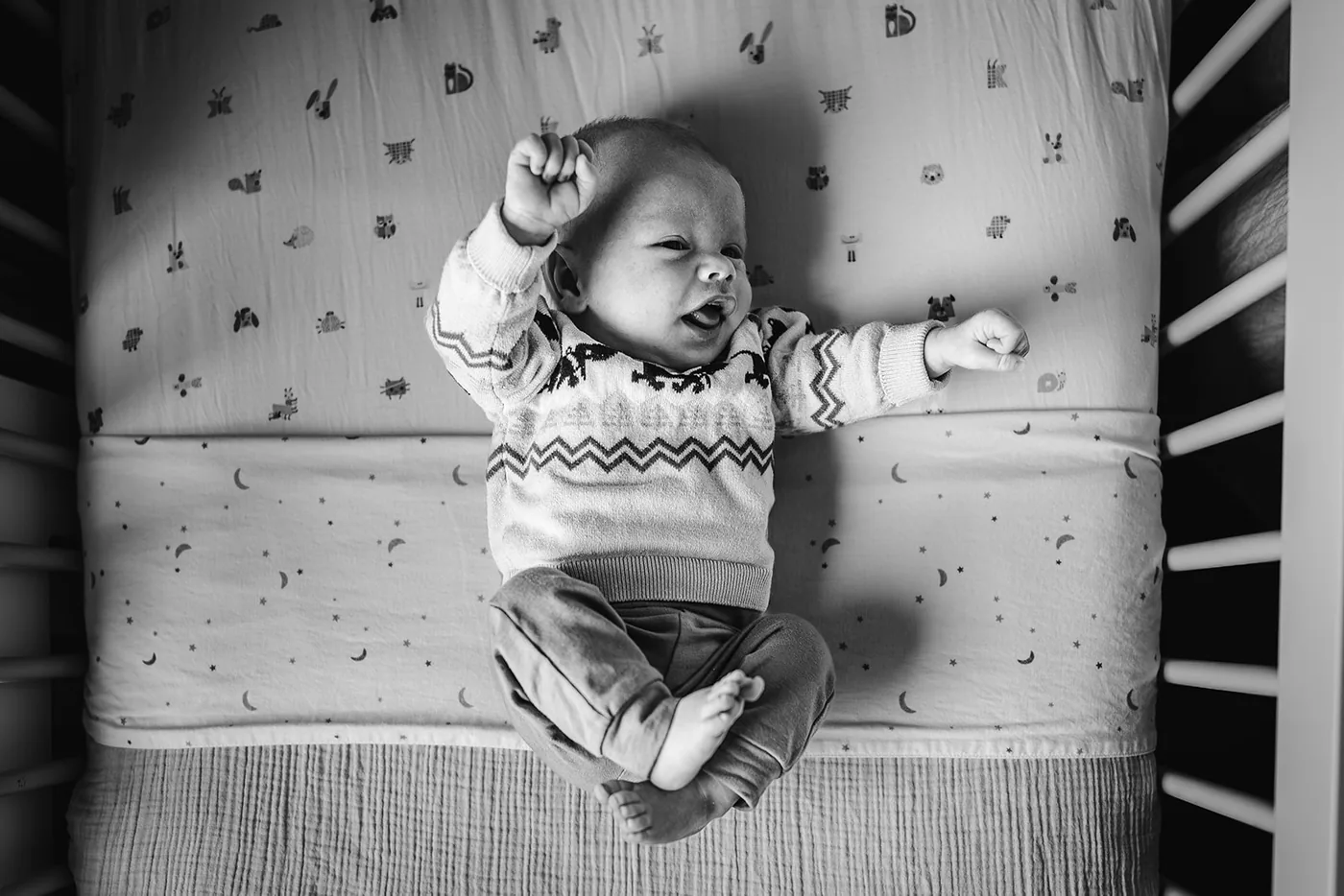 Zwart-wit: een baby ligt met gestrekt armpje in het ledikant
