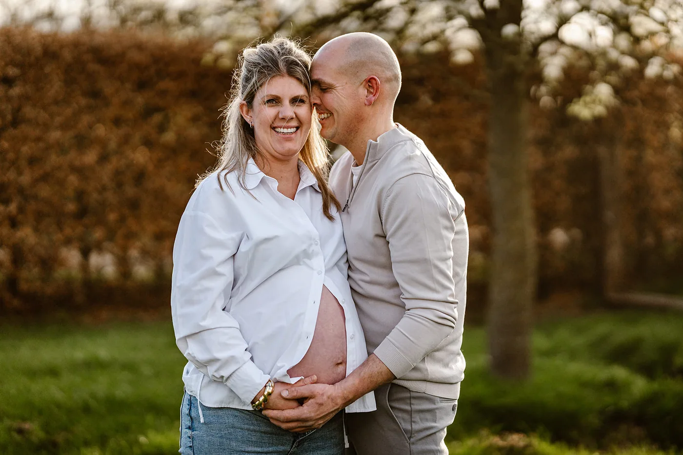 Aanstaande ouders met hun handen op de buik, in het avondlicht