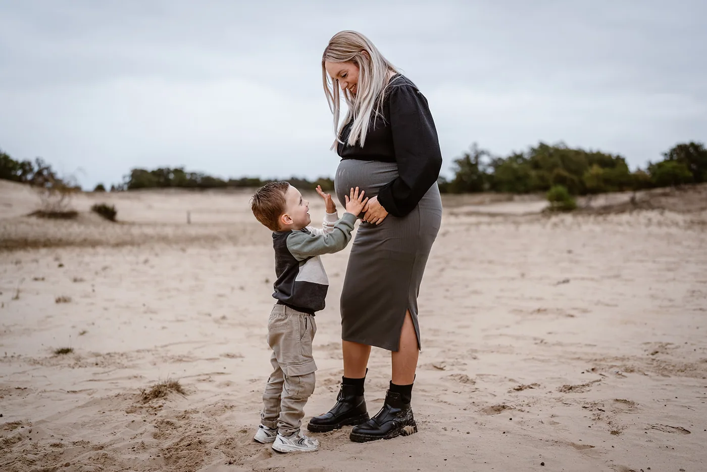 Kleine jongen legt zijn handen op de buik van zijn moeder, midden in het zand