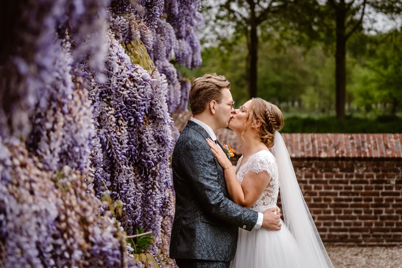 Bruidspaar kust elkaar onder een bloeiende blauweregen bij Buitenplaats Amerongen, trouwfotografie door TWP Weddings